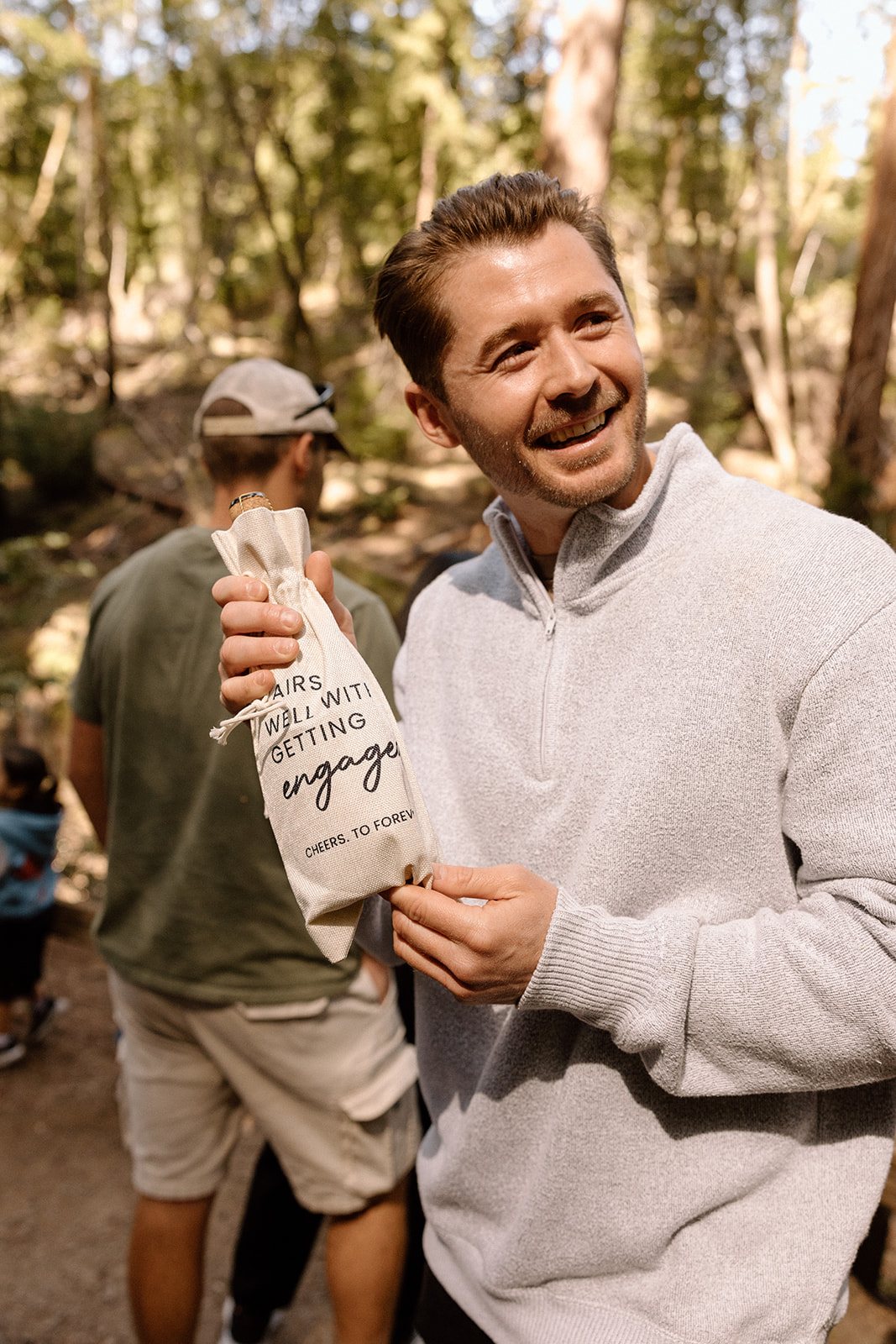 Abel grinning and holding a gift bag that reads Pairs well with getting engaged