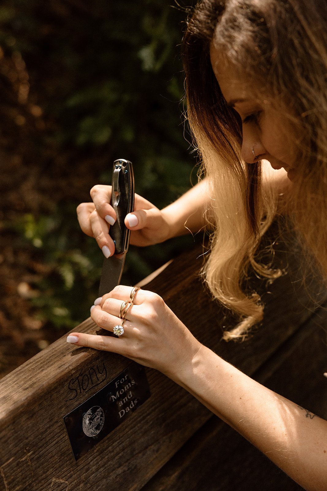 Aidan carving initials into the bench with a pocket knife, ring on her hand