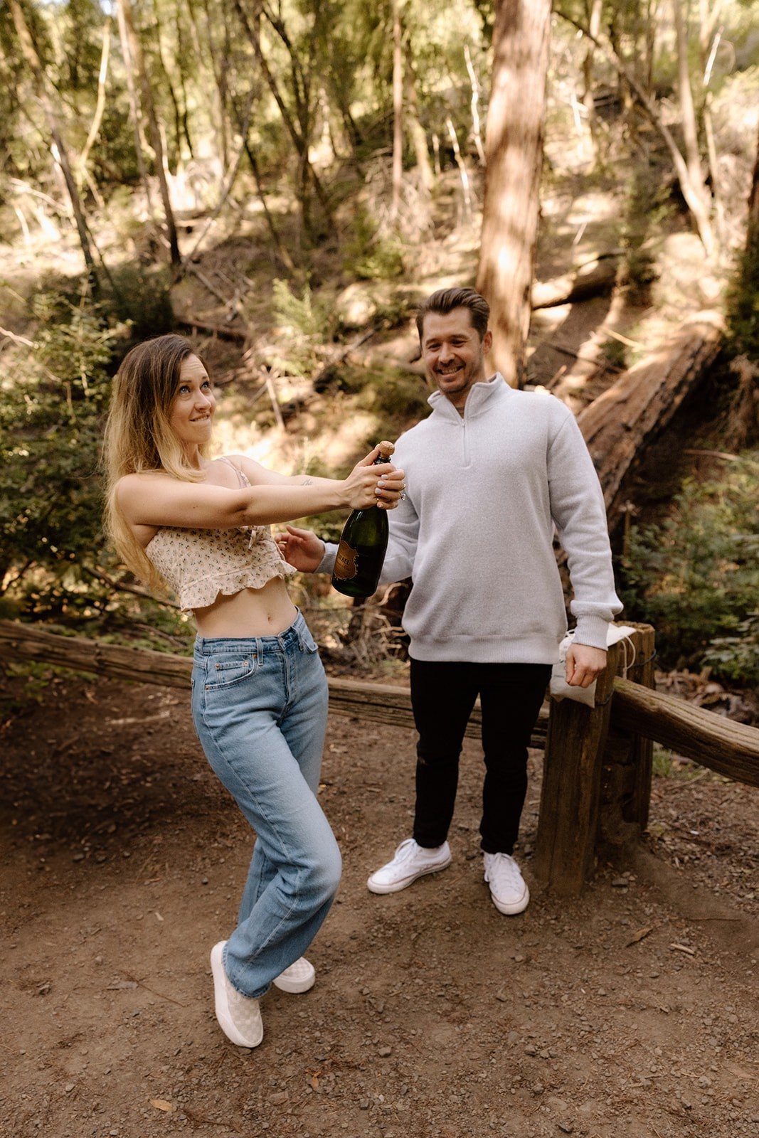 Aidan bracing to pop a champagne cork in the redwoods while Abel laughs